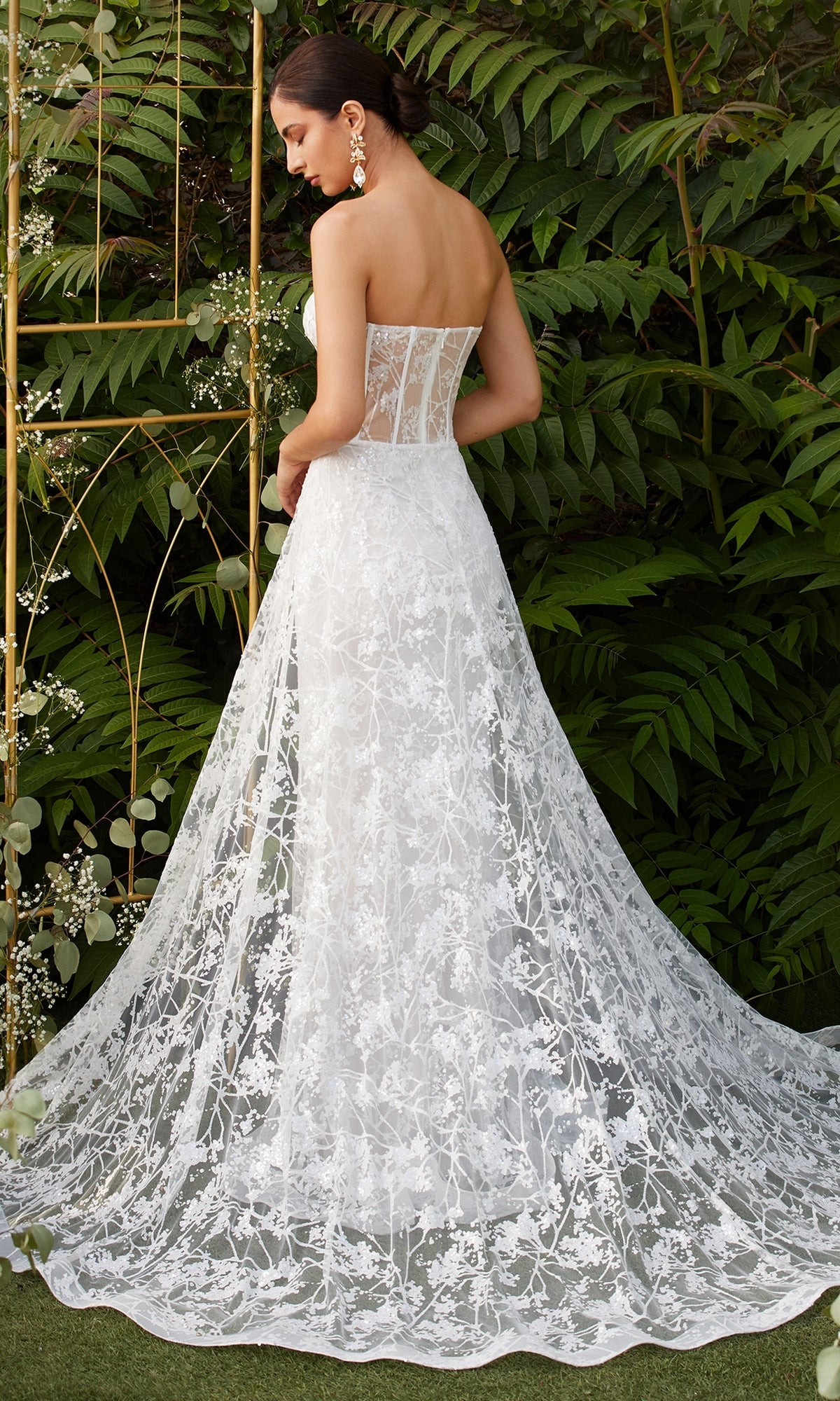 A woman in the Strapless Long White Wedding Dress CB046W, featuring floral embroidery and a sheer corset back, stands outdoors in front of green foliage.